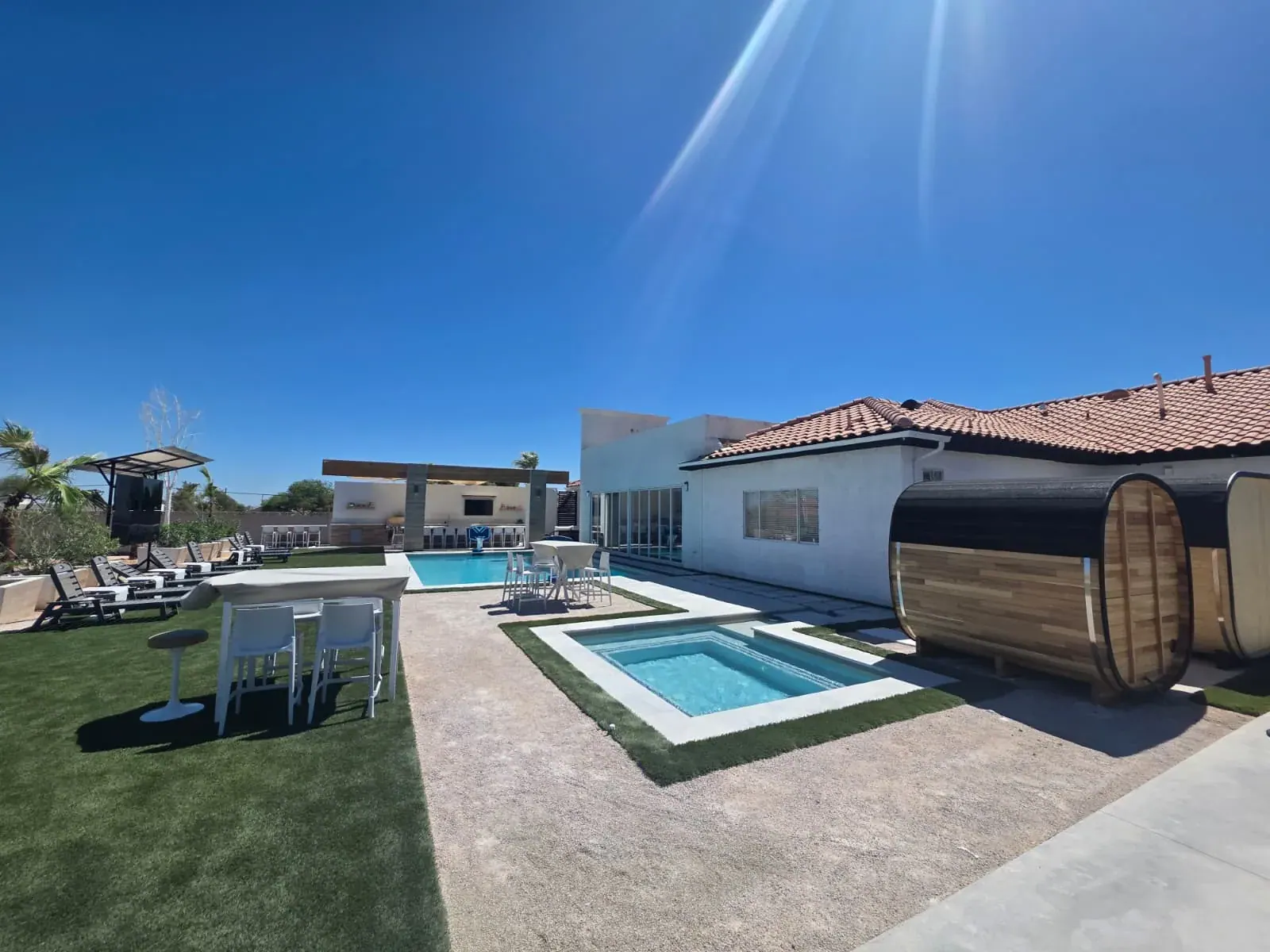 The villa’s backyard — pool, sunken spa, a cedar barrel sauna, the shaded outdoor kitchen and rows of loungers across the lawn