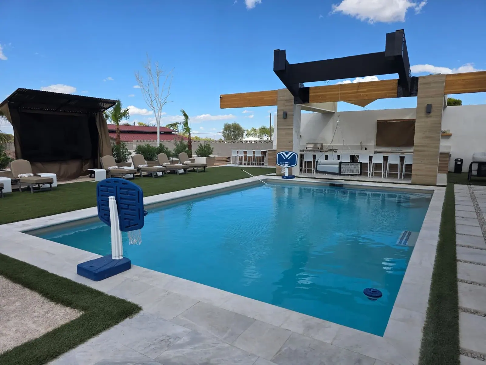 The villa’s private pool on a clear day — the pergola-covered outdoor kitchen and hibachi bar at the far end and a row of loungers along the lawn