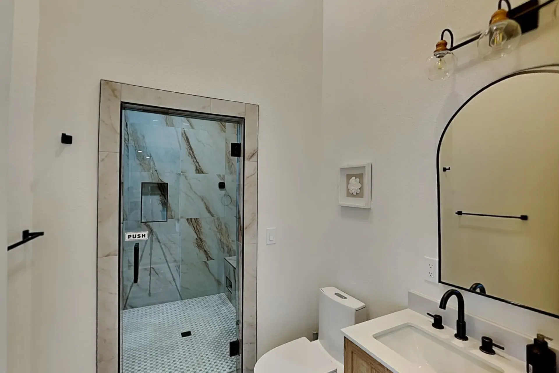 Full bathroom with a marble-tiled shower behind a glass door, an oak vanity and an arched mirror