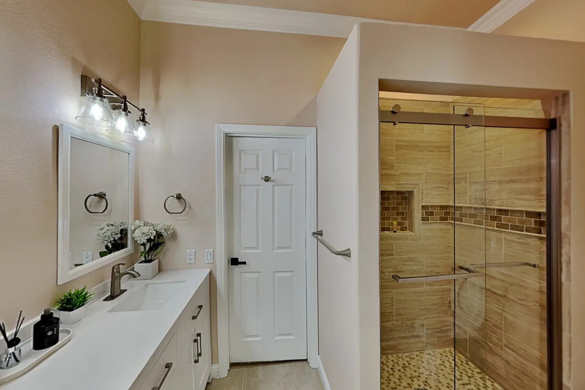 Full bathroom with a long white vanity and a travertine shower behind sliding glass