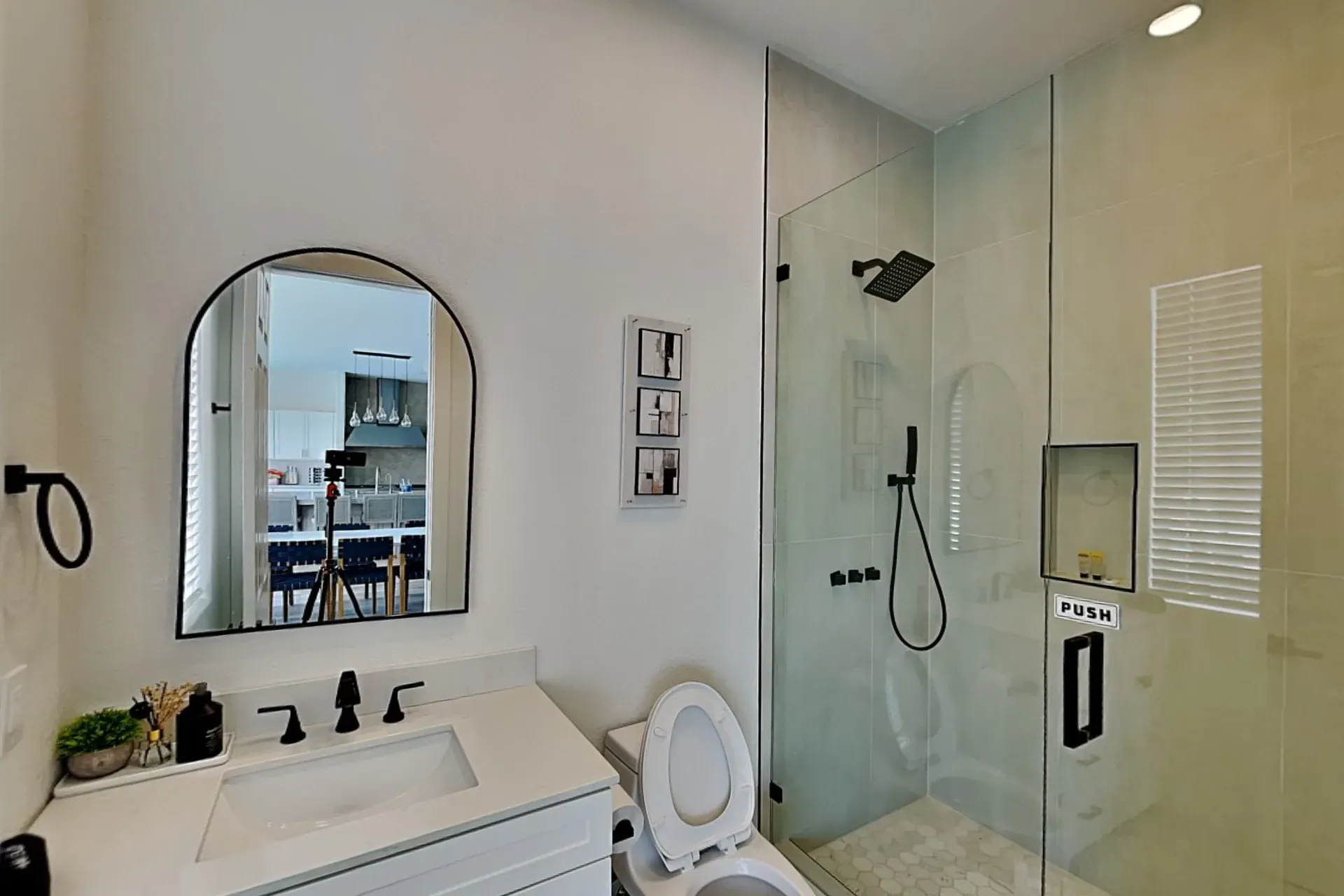 Full bathroom with an arched black-framed mirror, quartz vanity and a glass walk-in shower with a rainfall head