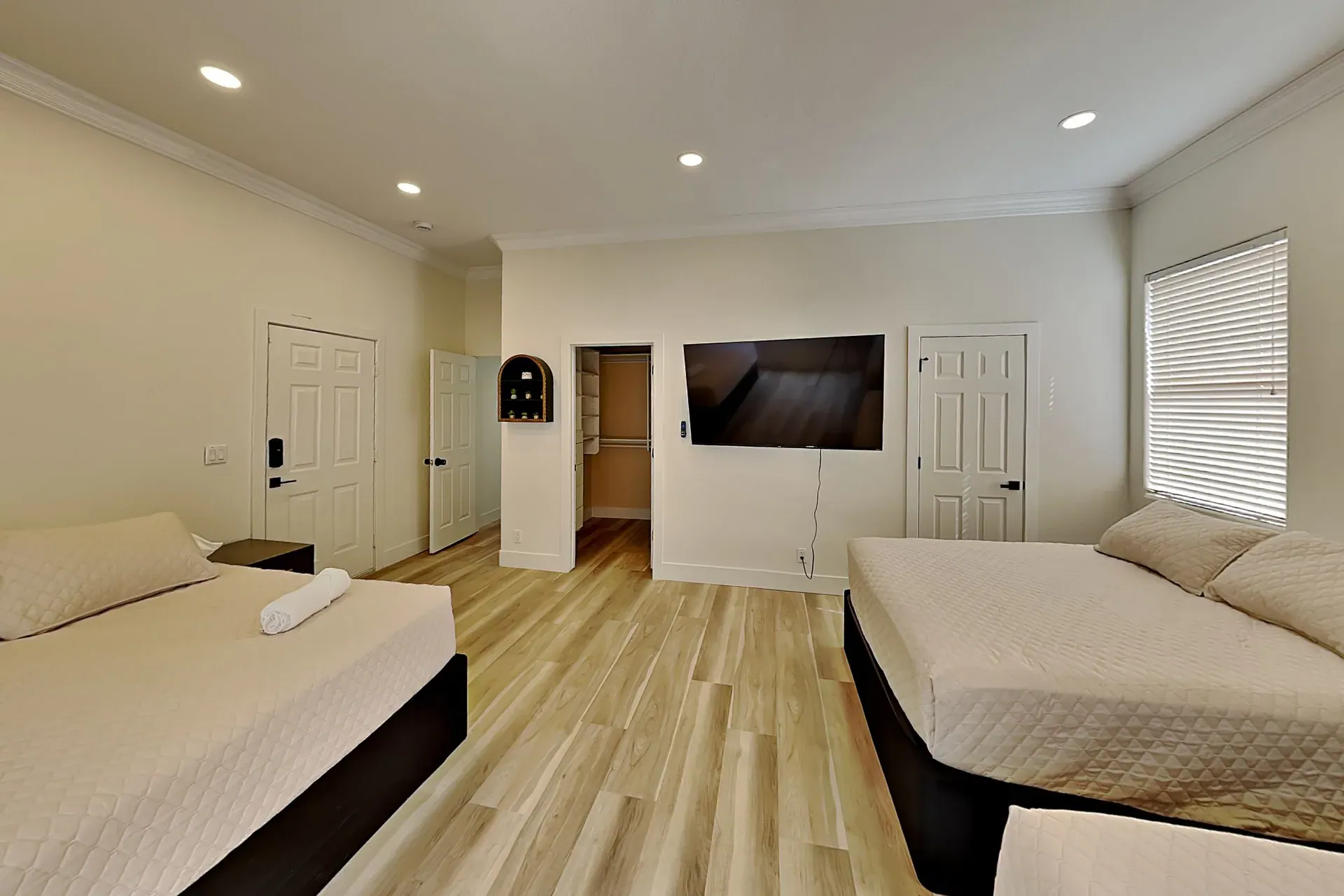 A guest bedroom with two beds, a wall-mounted TV and a walk-in closet