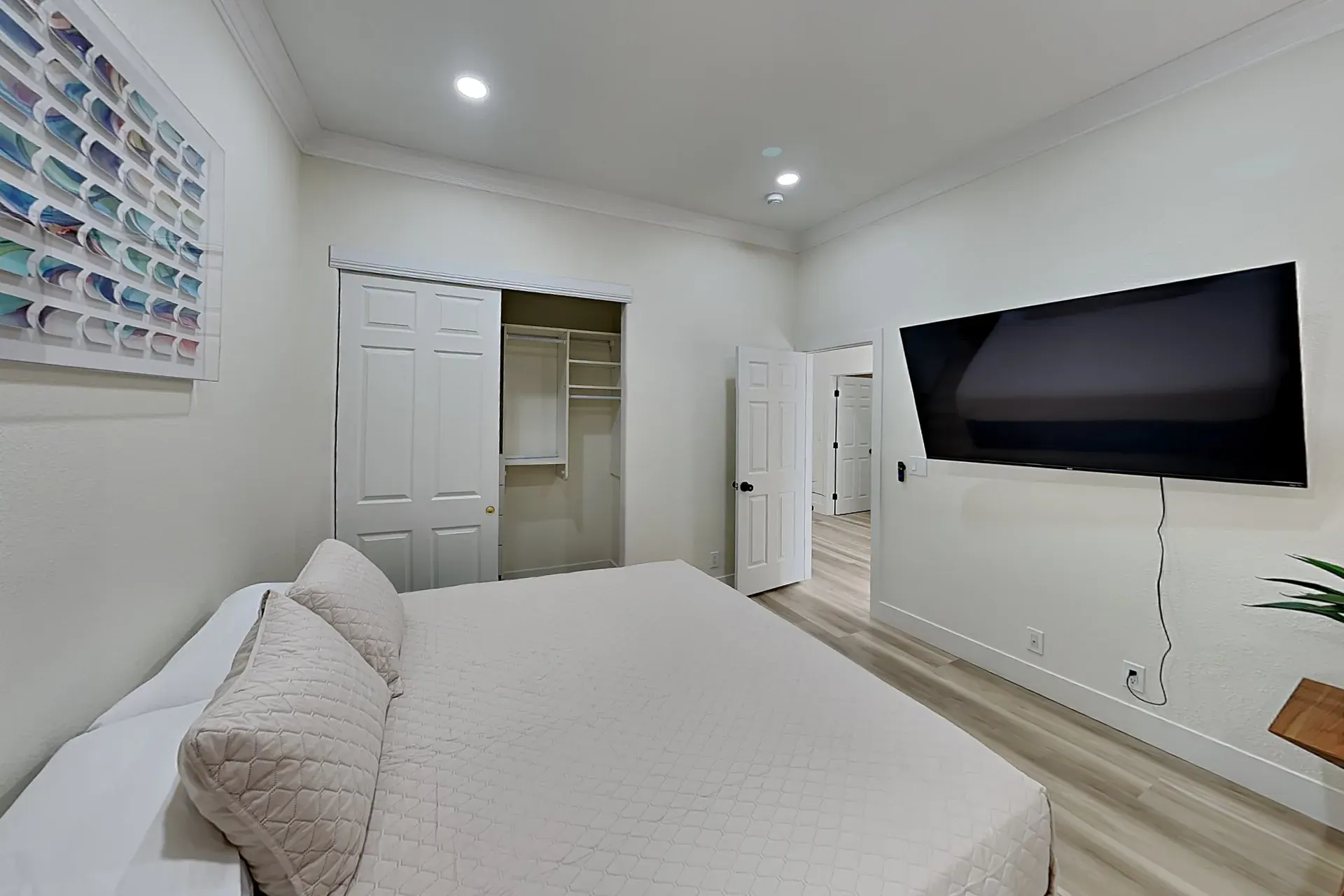 A guest bedroom with a wide wall-mounted TV and a mirrored closet