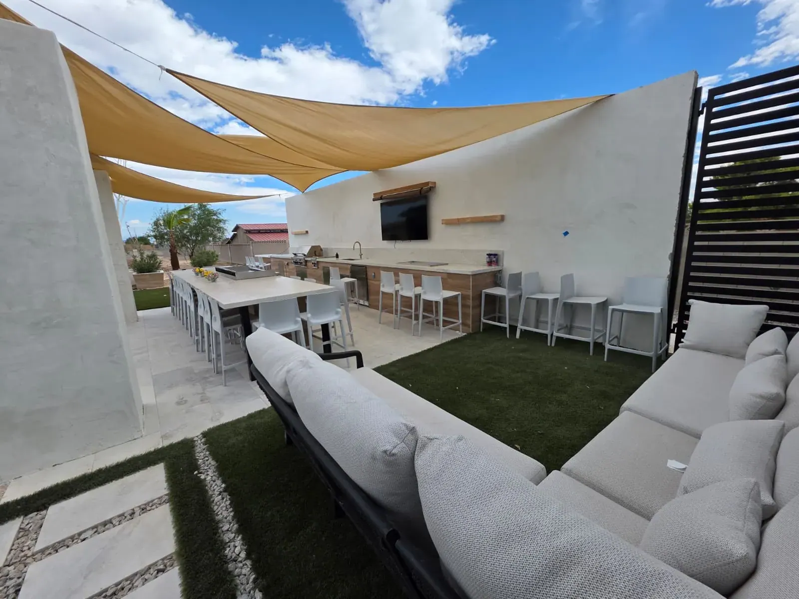 Covered courtyard lounge with a wraparound sectional and outdoor TV under shade sails
