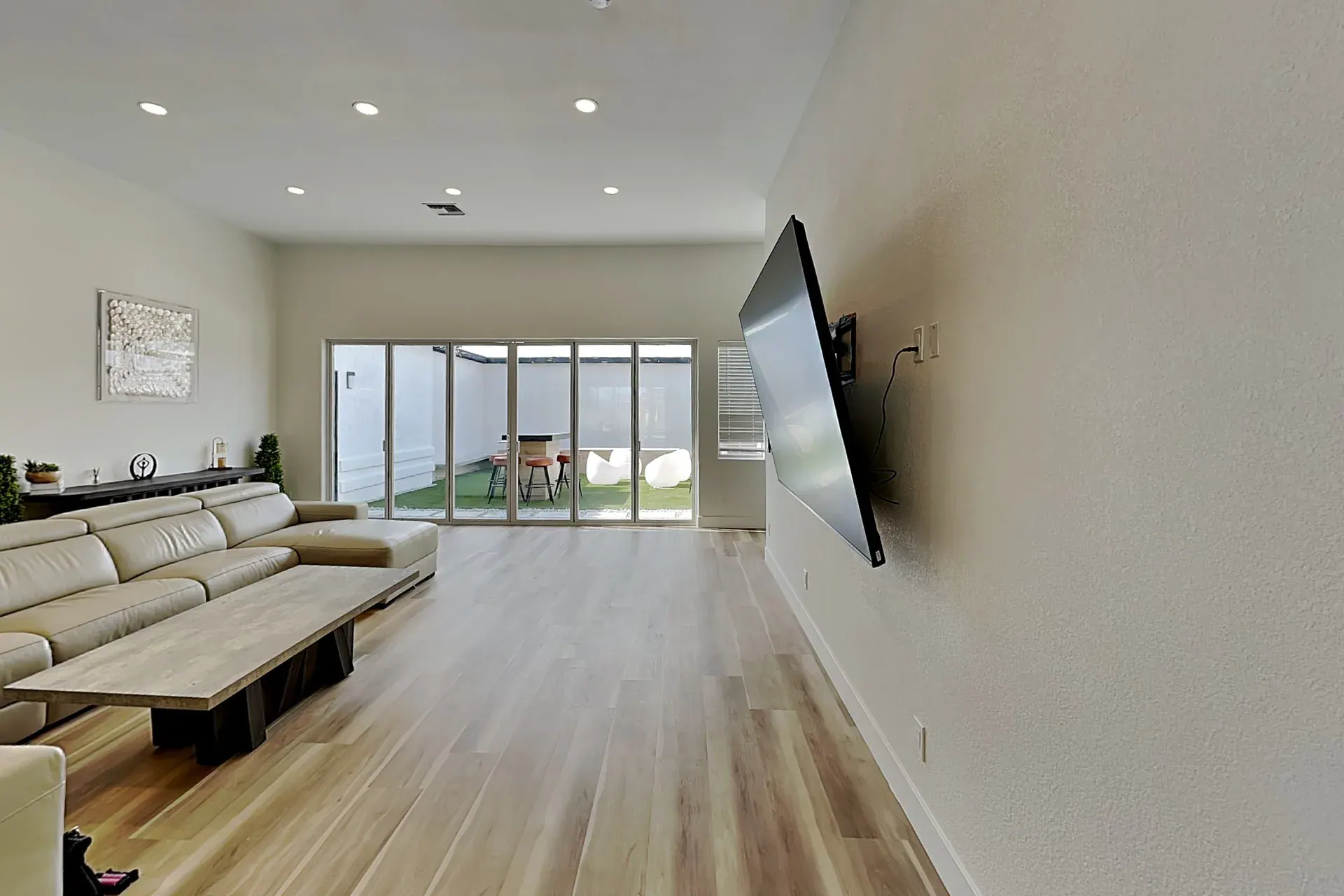 The second living room, its own wall-mounted screen facing a long sectional, with sliding glass out to the courtyard