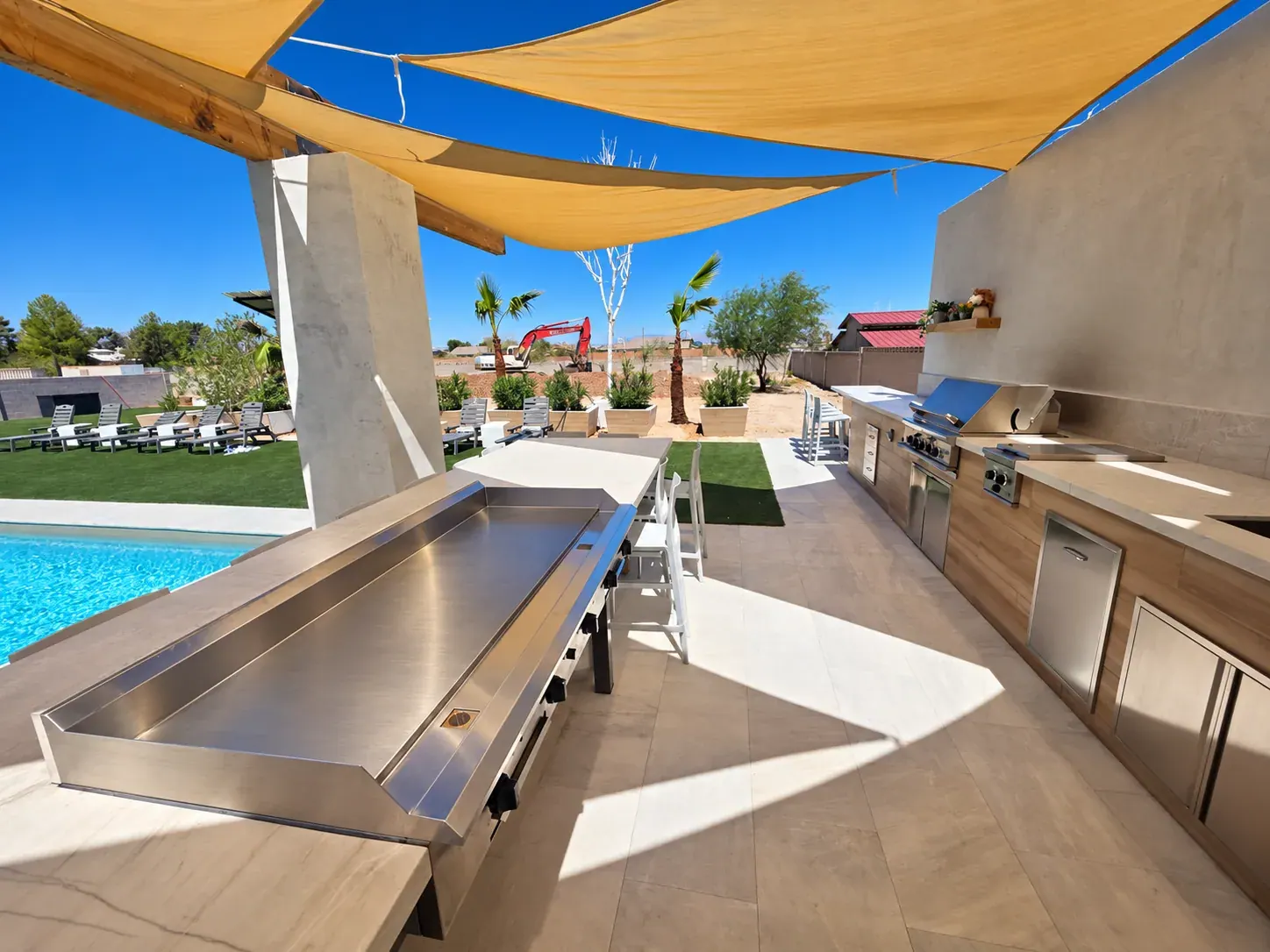 The 60-inch built-in hibachi griddle set into the outdoor kitchen bar under shade sails, with the built-in BBQ and side burners along the counter