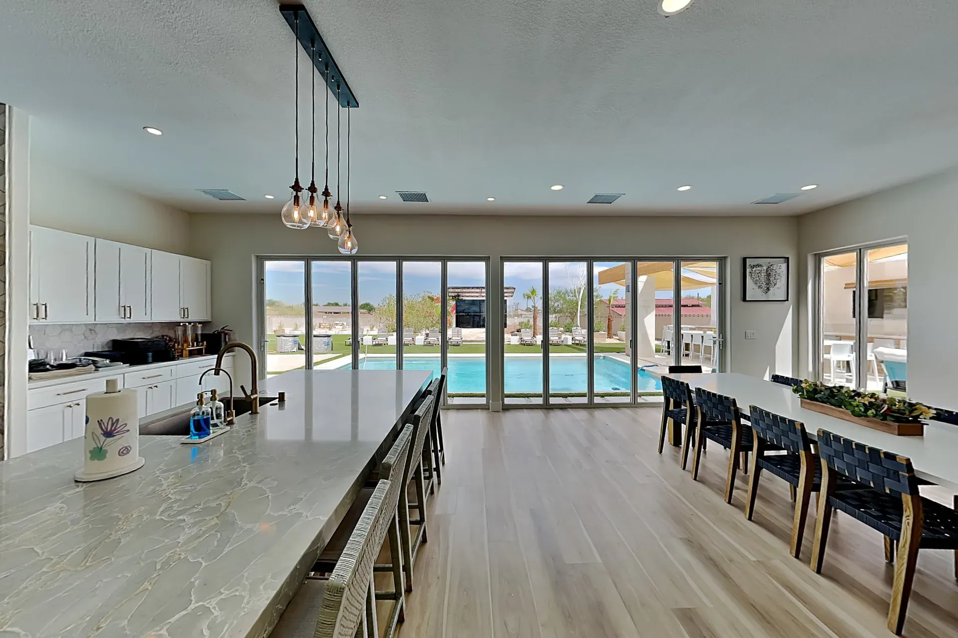 The kitchen and dining room looking out through a full glass wall to the pool, the long dining table set for the group