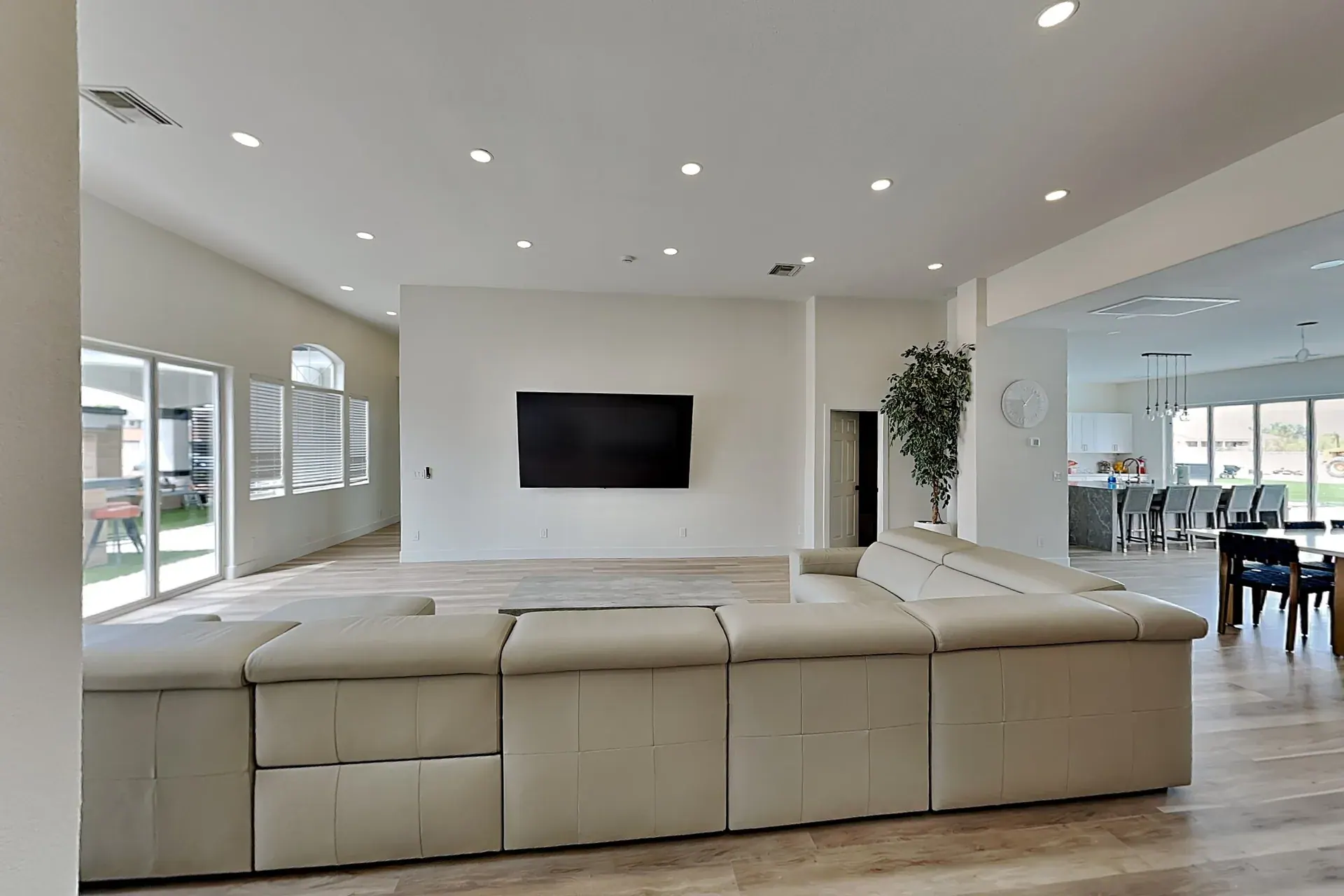 The main living room — a deep sectional facing the 100-inch screen, open through to the kitchen