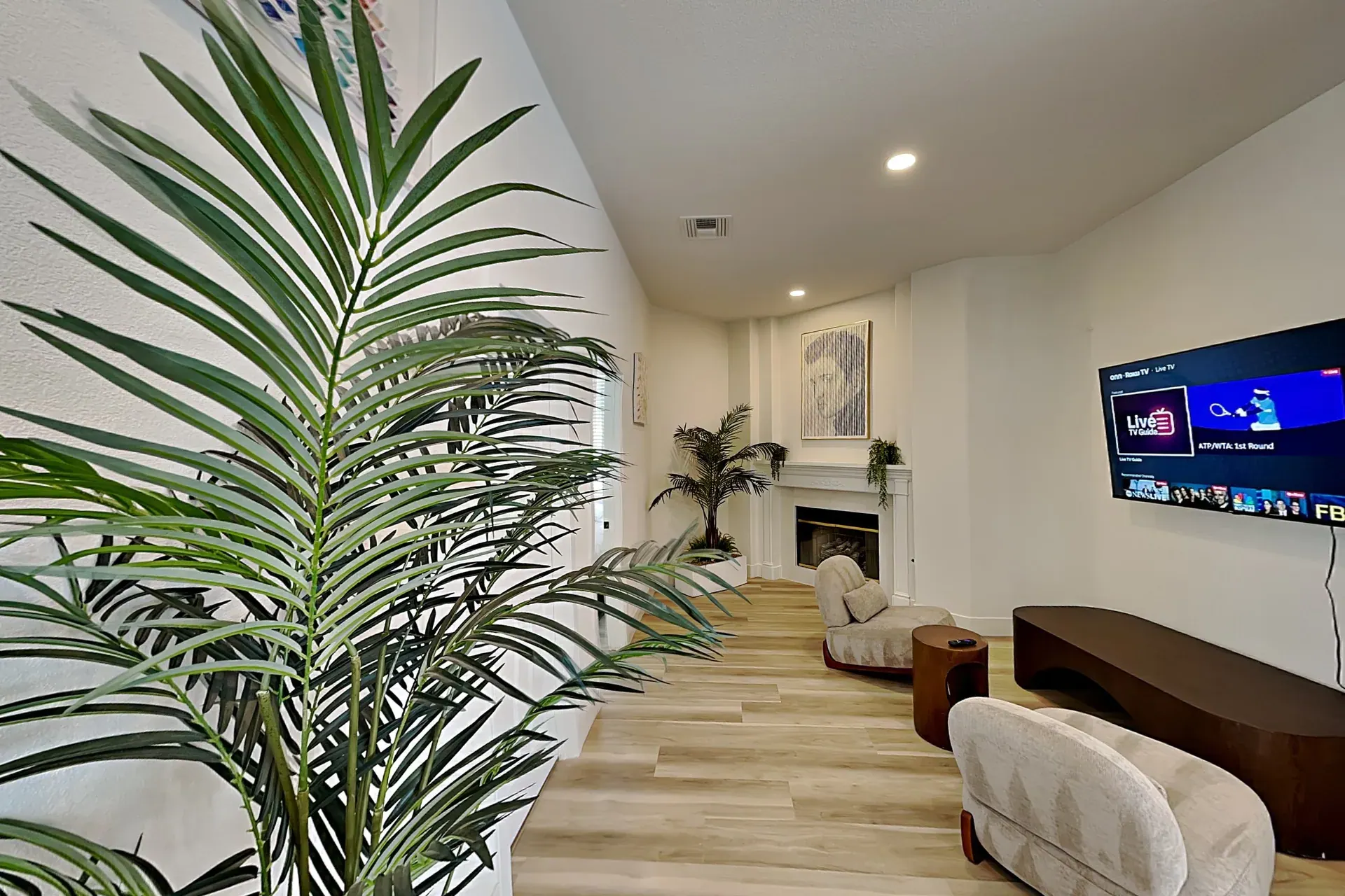 A quieter sitting room with a fireplace, curved lounge chairs, a low bench and a wall-mounted TV
