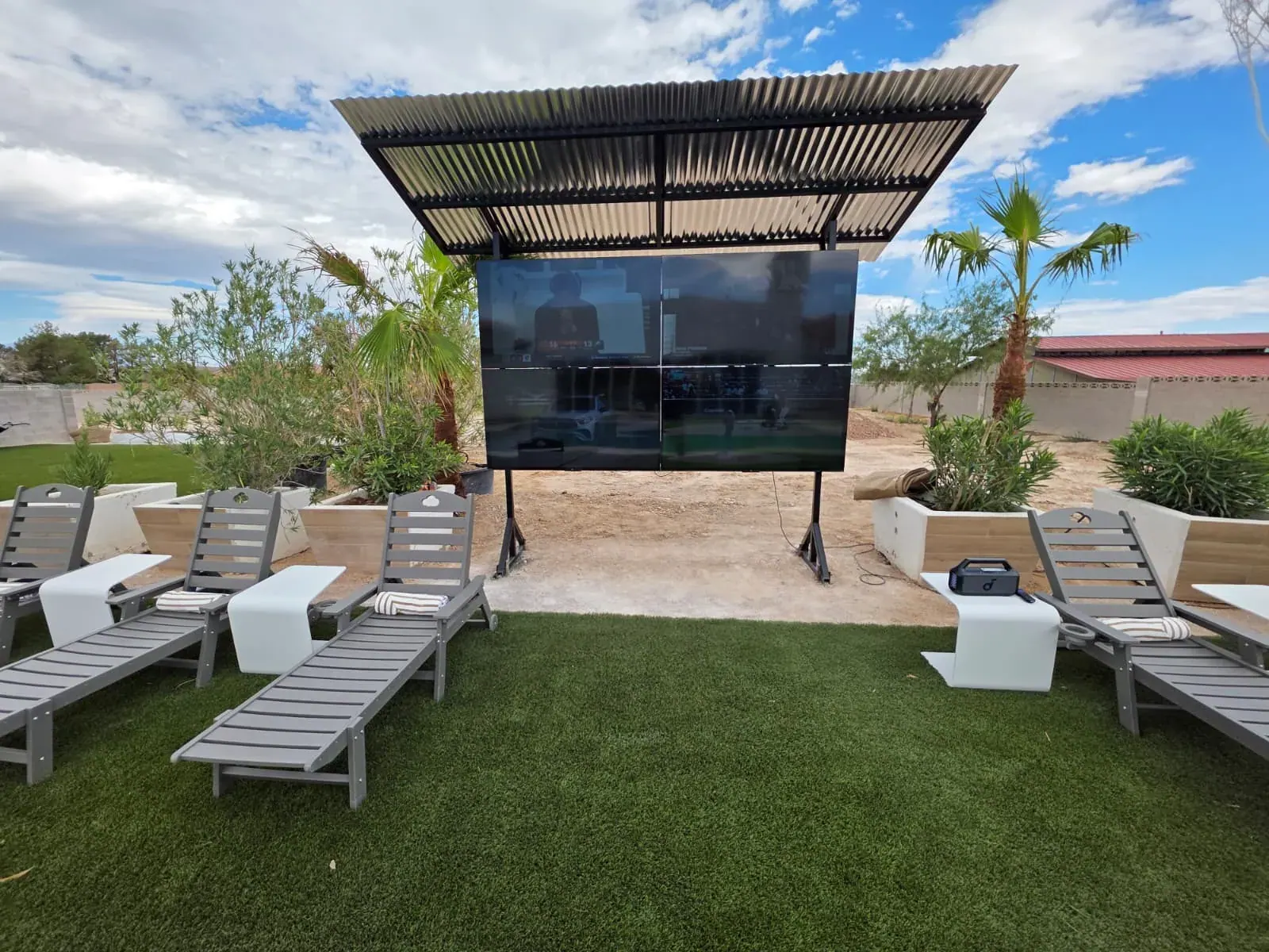 The outdoor theater — a four-panel video wall under a steel canopy, faced by a row of loungers on the lawn