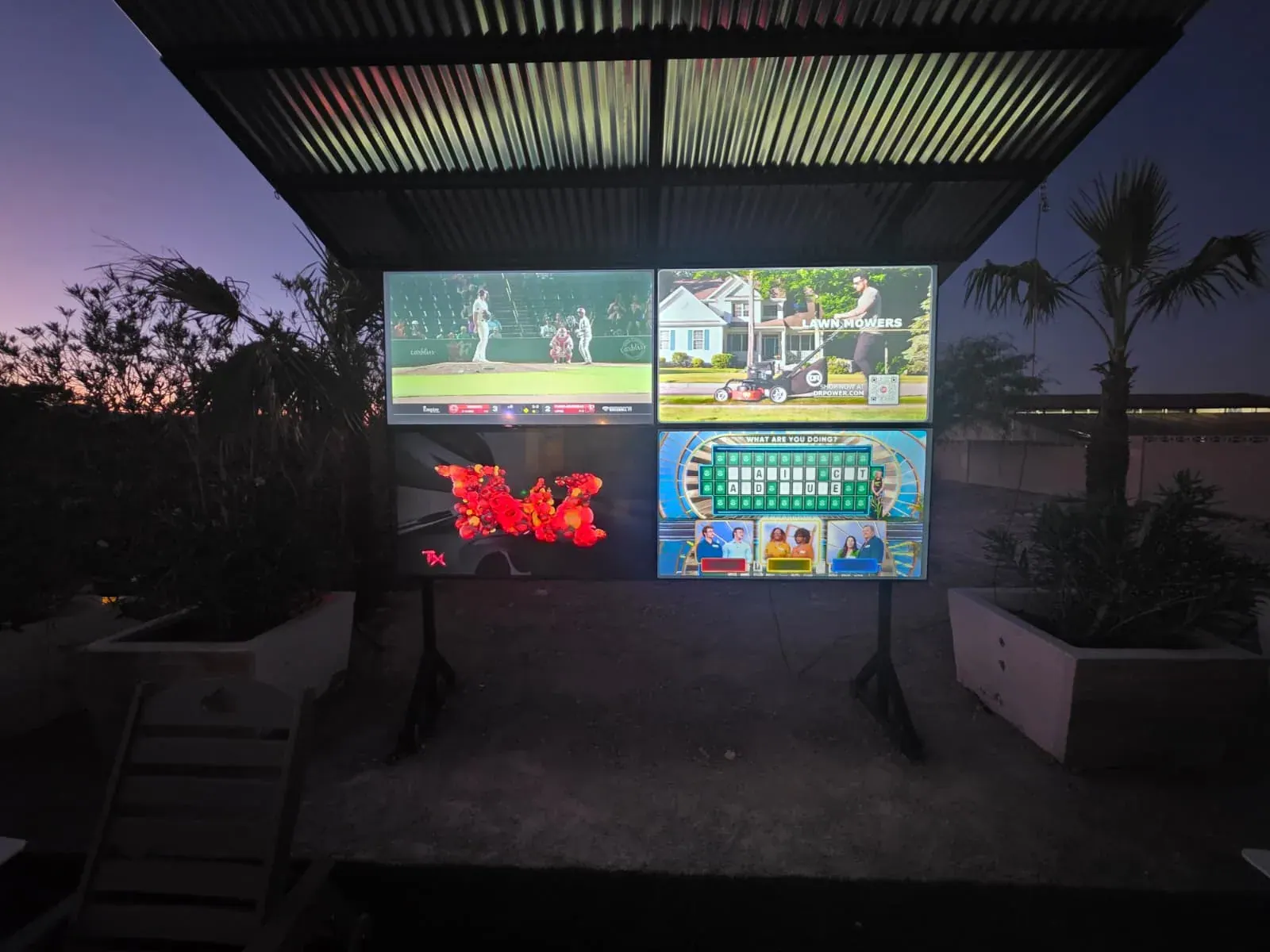 The outdoor theater at dusk — four 65-inch screens each running a different programme
