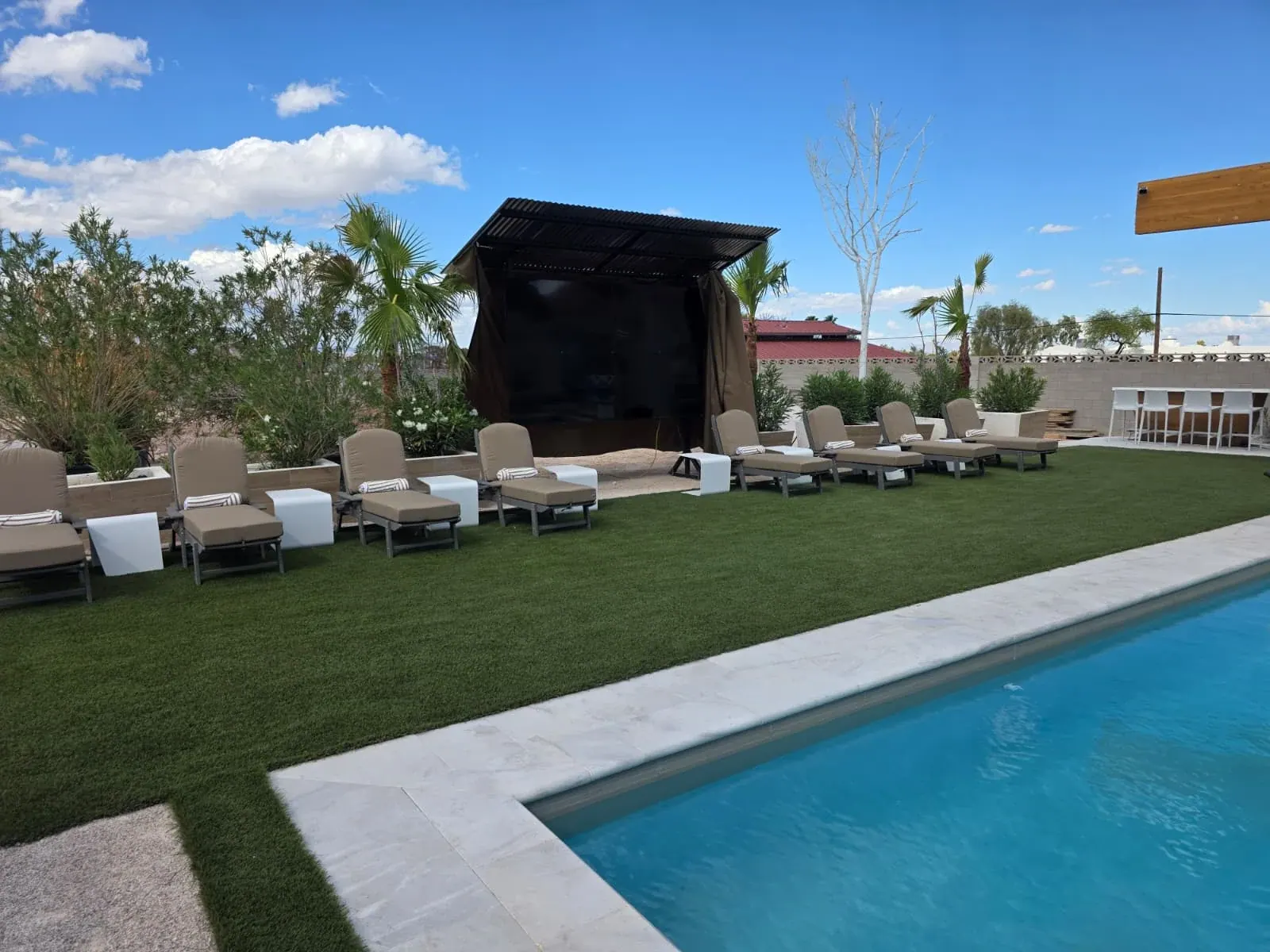 The outdoor theater seen from the pool’s edge, loungers lined up on the lawn in front of it