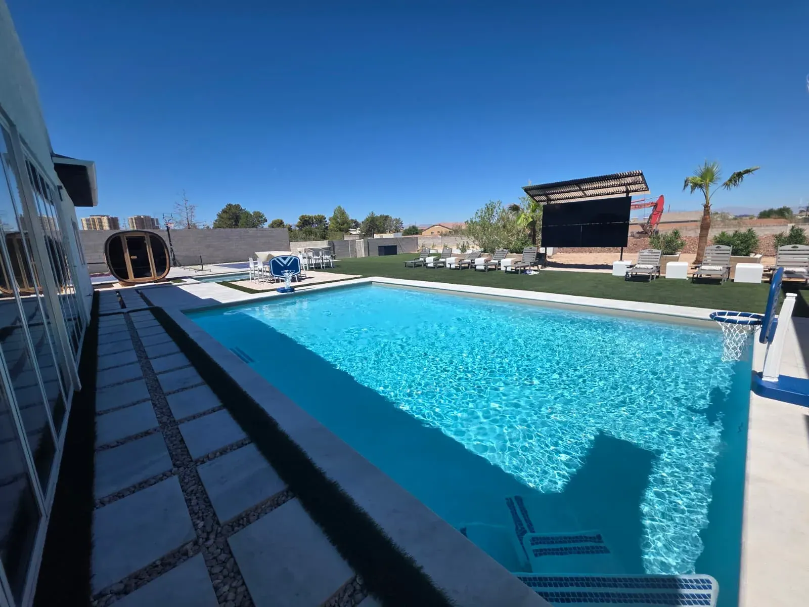 The private pool under a clear desert sky, with a barrel sauna, the poolside basketball hoop and the outdoor theater screen on the lawn beyond