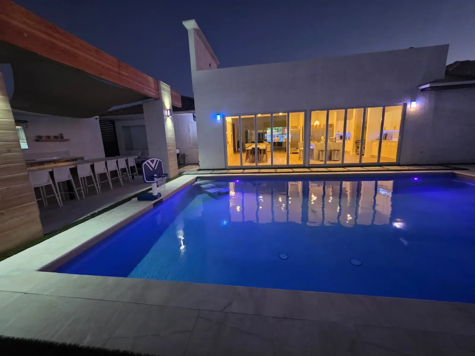 The pool lit blue after dark, the villa’s glass wall glowing behind it and the hibachi bar under its pergola to one side