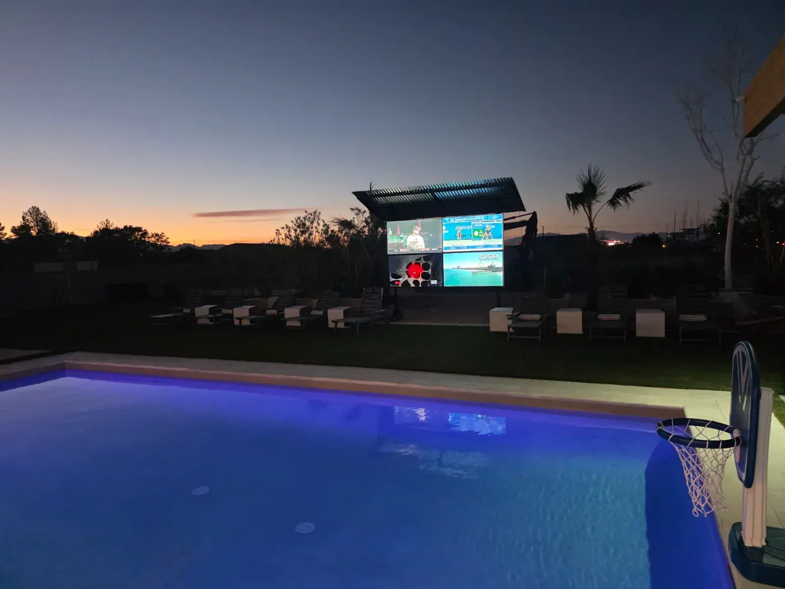 The pool at dusk with the four-screen outdoor theater lit up across the lawn