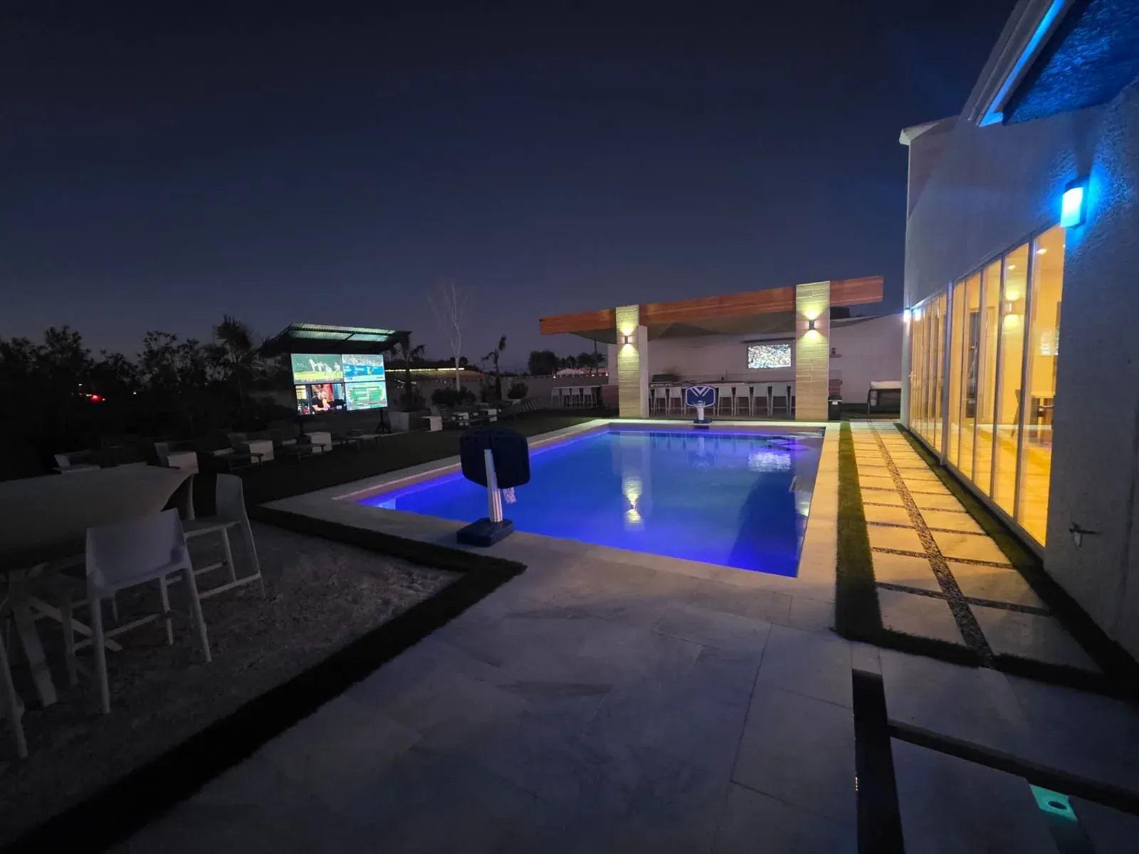 The pool glowing blue at night, four different programmes running on the outdoor video wall across the lawn