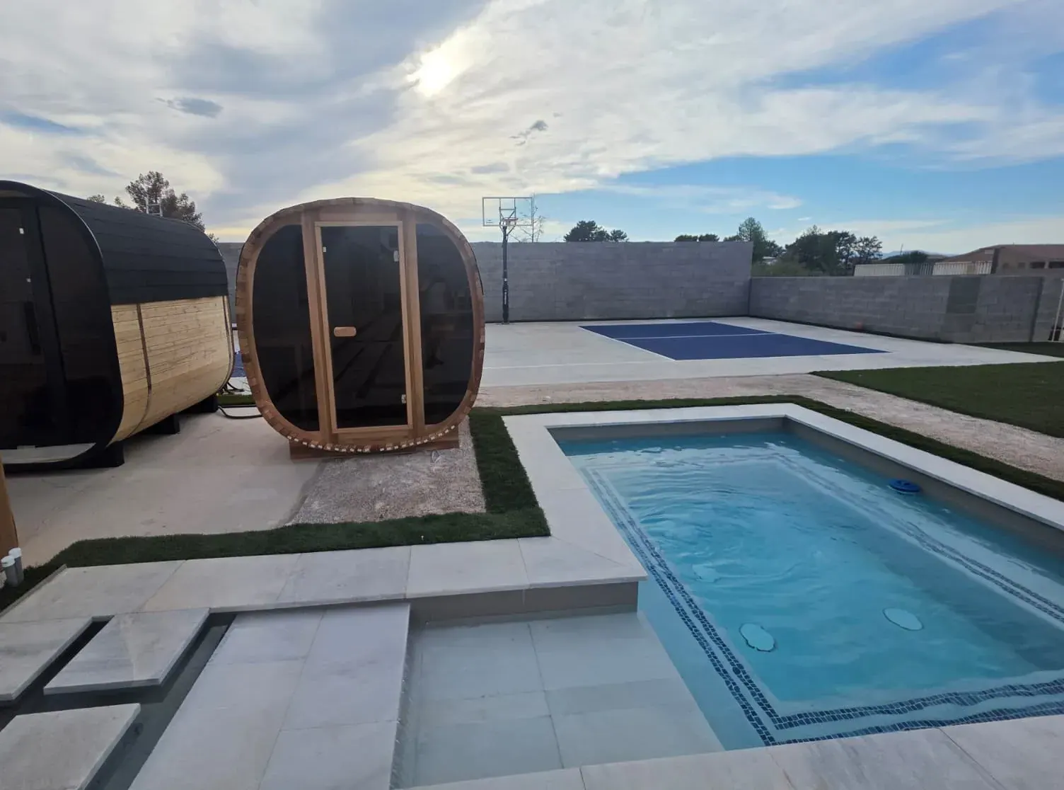 The two outdoor cedar dry saunas beside the cold plunge pool, with the sports court beyond