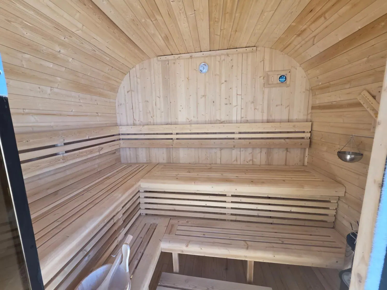 Inside one of the dry saunas — tiered pale-pine benches, backrest, thermometer and water bucket
