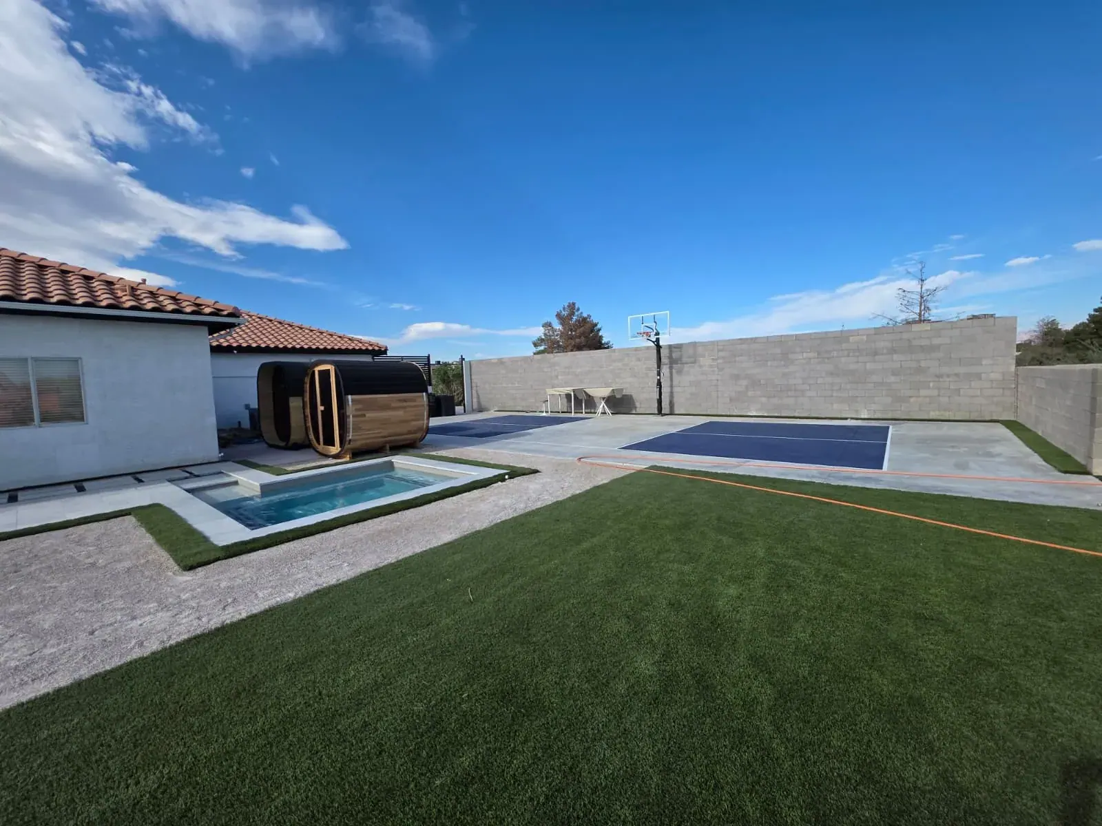The private sports court with basketball hoop, beside the barrel saunas and cold plunge